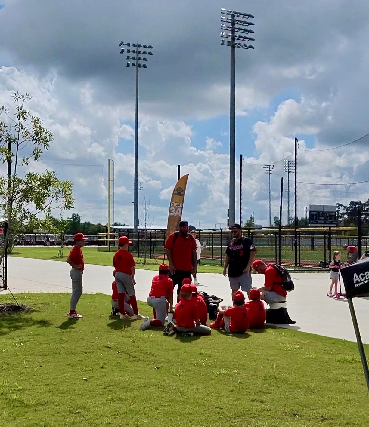 Redbirds players in red gathered on the grass with their coaches beside the Field 3A banner